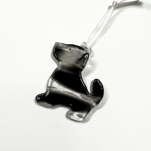 May include: A black and white striped glass ornament shaped like a dog with a white ribbon attached.