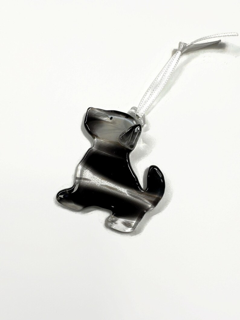 May include: A black and white striped glass ornament shaped like a dog with a white ribbon attached.
