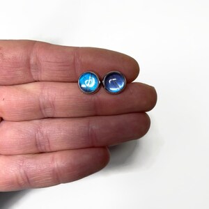 May include: A pair of silver stud earrings with blue and purple butterfly wing designs.