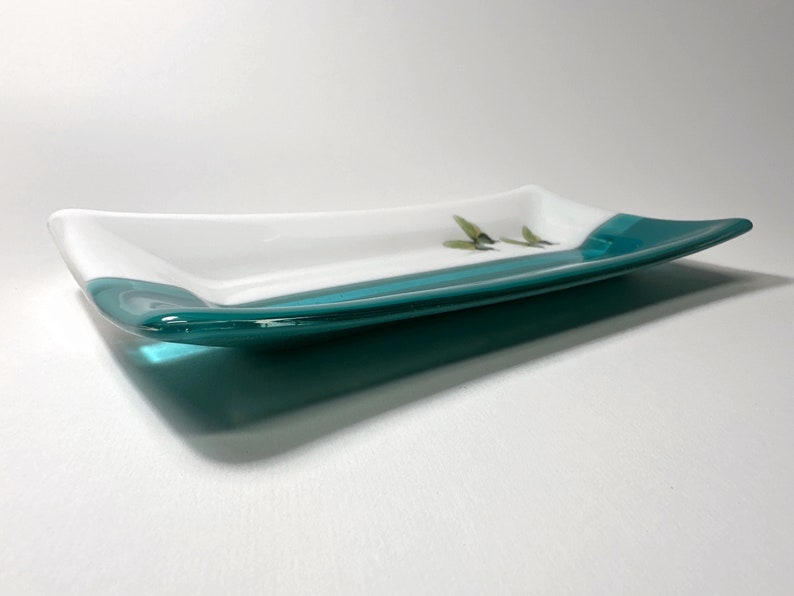 May include: A rectangular glass serving dish with a white interior and a teal blue rim. The dish is slightly curved and has a glossy finish.