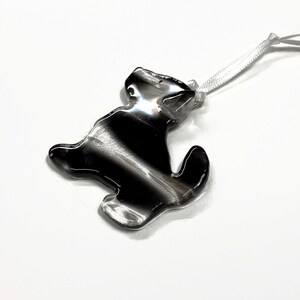 May include: A black and white glass ornament shaped like a dog with a white ribbon attached.