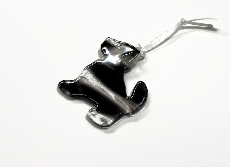 May include: A black and white glass ornament shaped like a dog with a white ribbon attached.