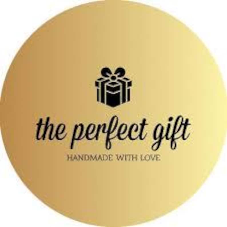 May include: A gold circle with a black gift box and bow in the center. The text "the perfect gift" is written in a black cursive font below the gift box. The text "handmade with love" is written in a smaller black font below the cursive text.