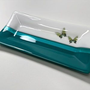 May include: A rectangular glass dish with a teal blue bottom and a white top. The dish has a white stripe across the middle and two green butterflies on the white surface.