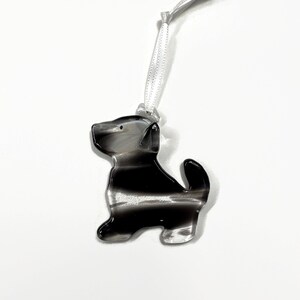 May include: A black and white striped glass ornament shaped like a dog. The ornament has a white ribbon for hanging.