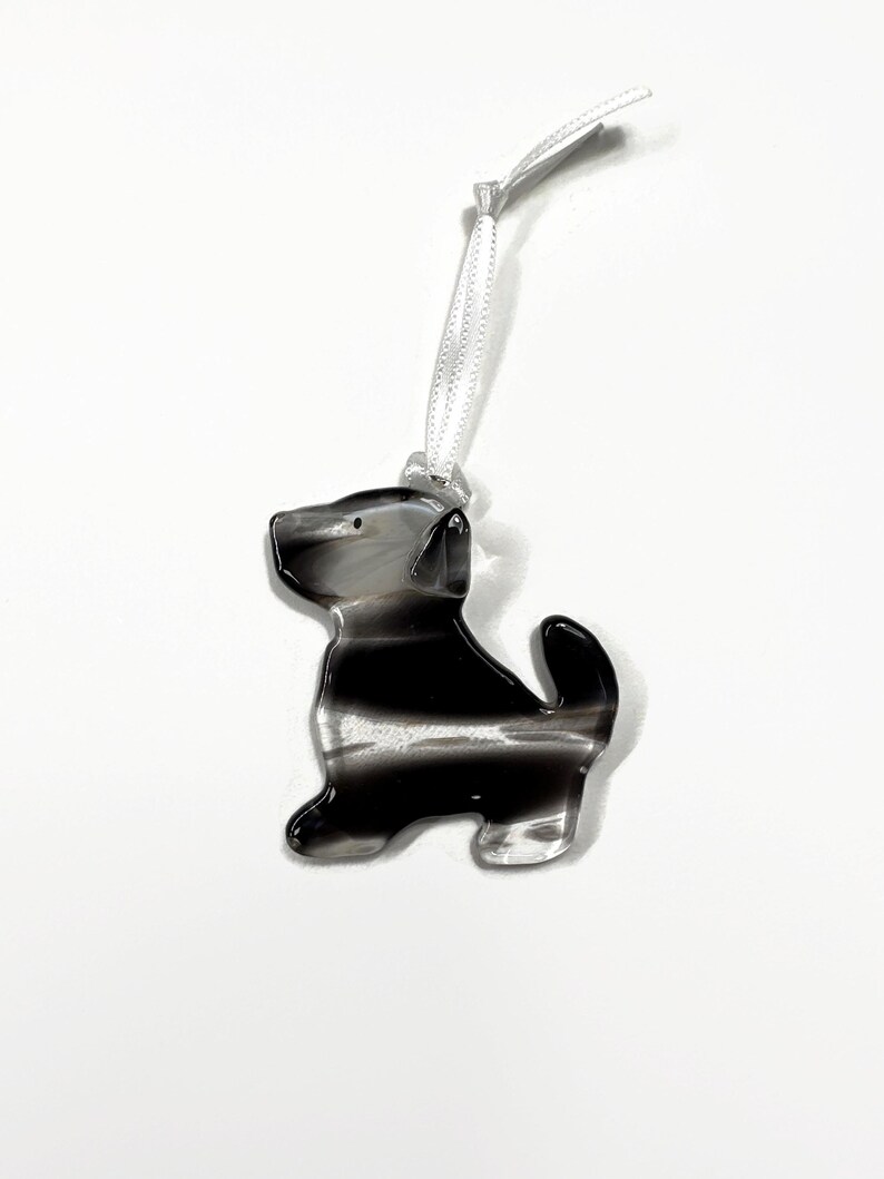 May include: A black and white striped glass ornament shaped like a dog. The ornament has a white ribbon for hanging.