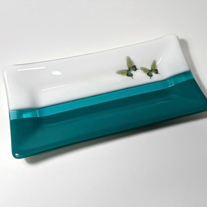 May include: A rectangular glass dish with a white top and a teal bottom. Two green butterflies are painted on the white surface.