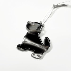 May include: Black and white striped glass ornament shaped like a dog with a white ribbon attached.