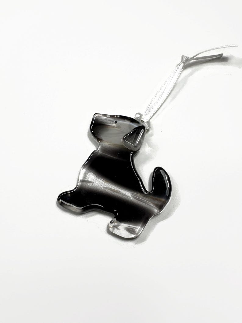 May include: Black and white striped glass ornament shaped like a dog with a white ribbon attached.
