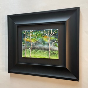 Puede incluir: Una obra de arte de cer&aacute;mica enmarcada que representa una escena de bosque con tres &aacute;rboles, una zona verde de hierba y un cielo azul y verde. Los &aacute;rboles tienen troncos y ramas blancas con hojas verdes. El cielo tiene un fondo azul claro con una nube azul oscura y verde.
