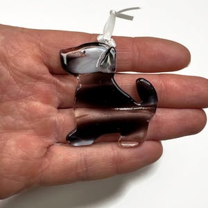 May include: A glass ornament shaped like a black and white dog with a white ribbon on its head.