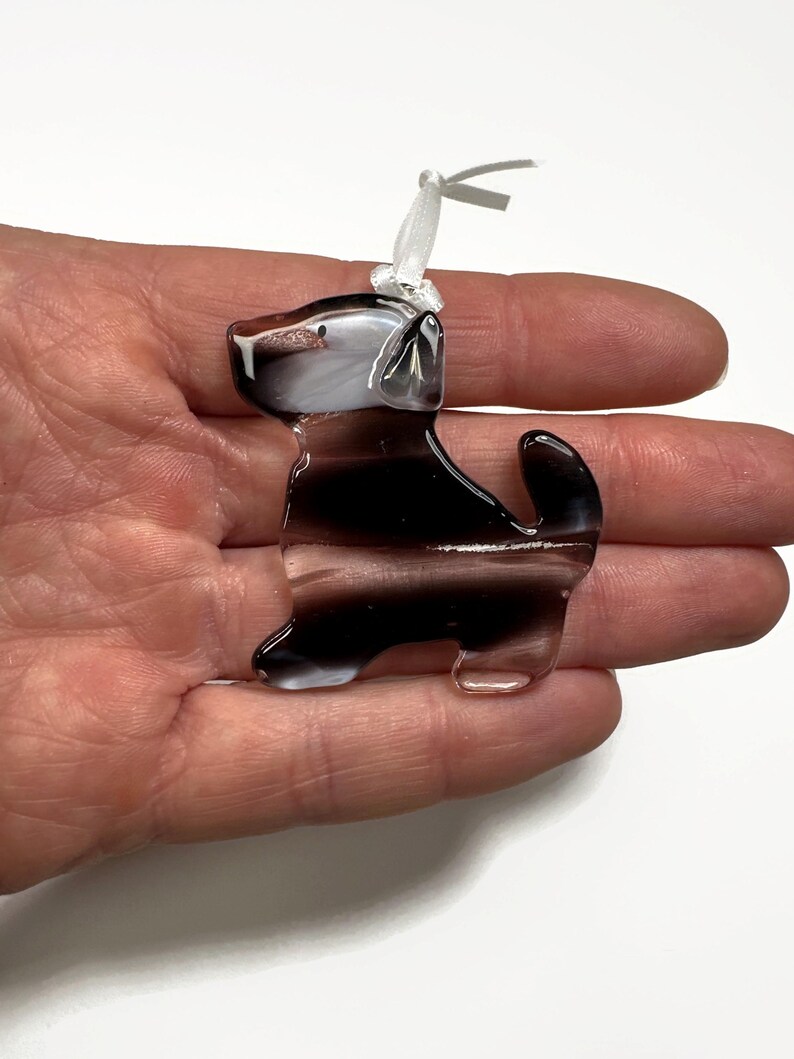 May include: A glass ornament shaped like a black and white dog with a white ribbon on its head.