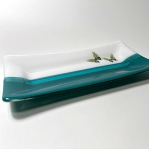 May include: A rectangular glass serving dish with a white top and a teal bottom. The dish has a hummingbird design on the white surface.