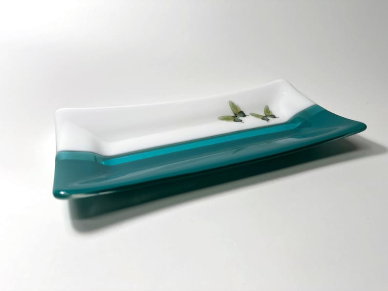 May include: A rectangular glass serving dish with a white top and a teal bottom. The dish has a hummingbird design on the white surface.
