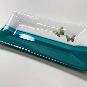 May include: A rectangular glass dish with a teal blue bottom and a white top. The dish has a white stripe across the middle and two green butterflies on the white section.