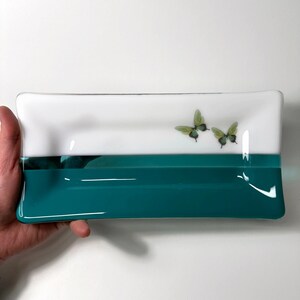 May include: A rectangular glass dish with a white top and a teal bottom. Two green butterflies are painted on the white top.