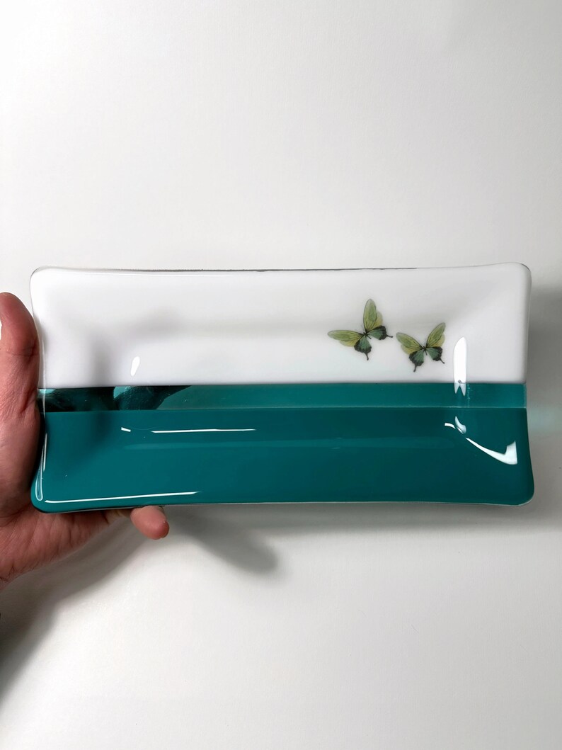May include: A rectangular glass dish with a white top and a teal bottom. Two green butterflies are painted on the white top.