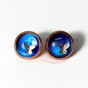 Puede incluir: Un par de pendientes de botón de oro rosa con un diseño de mariposa azul y blanca.