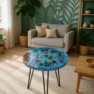 Puede incluir: Mesa de centro redonda con una tapa de resina azul con un diseño de vida marina. La mesa tiene patas de horquilla de metal negro. El diámetro de la mesa es de aproximadamente 61 cm.