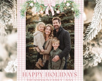 May include: A holiday card with a family photo, framed by a pink and white gingham pattern. The card features the text "Happy Holidays" and "The Johnson Family 20XX". A watercolor garland with a pink bow and greenery decorates the top.