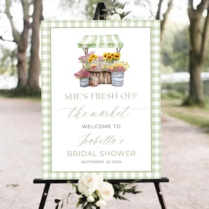 Peut inclure: Panneau de bienvenue pour une fête prénuptiale avec une bordure vichy verte et blanche. Il présente une illustration à l'aquarelle d'un stand de fleurs avec des tournesols et d'autres fleurs. Le texte indique "She's Fresh Off the Market" et "Welcome to Isabella's Bridal Shower".