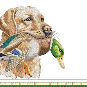 Może przedstawiać: Haftowany obraz złotego labradora trzymającego w pysku kaczora krzyżówkę. Kaczor ma zielone, brązowe, niebieskie i pomarańczowe detale. Sierść psa jest w kolorze jasnobrązowym, na białym tle.