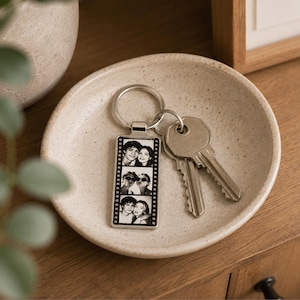 May include: A rectangular silver-toned metal keychain featuring a vertical film strip design with three black and white portrait photos of a couple. The keychain is attached to a circular metal ring holding two silver-colored metal keys.