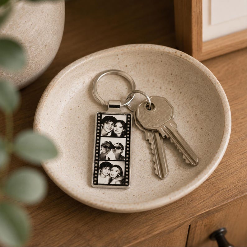 May include: A rectangular silver-toned metal keychain featuring a vertical film strip design with three black and white portrait photos of a couple. The keychain is attached to a circular metal ring holding two silver-colored metal keys.
