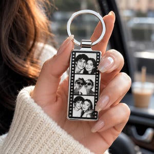 May include: A rectangular silver-toned metal keychain featuring a vertical film strip design. The center contains three stacked black and white photographs of a couple in different poses, enclosed within a frame with small square sprocket holes.