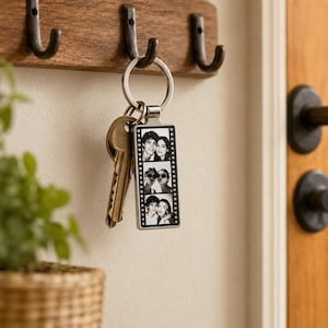 May include: A rectangular metal keychain featuring a vertical film strip design with three black and white portrait photos of two people. The keychain is attached to a silver split ring holding a single brass-colored metal key.