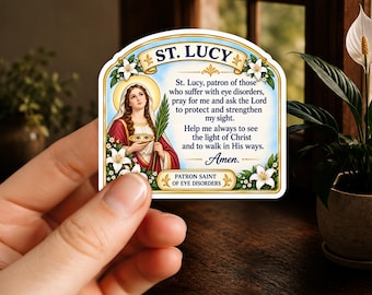 May include: A rectangular sticker with rounded top corners featuring an illustration of St. Lucy holding a palm branch and a dish with eyes. The text reads: St. Lucy, patron of those who suffer with eye disorders, pray for me and ask the Lord to protect and strengthen my sight. Help me always to see the light of Christ and to walk in His ways. Amen. Patron Saint of Eye Disorders.