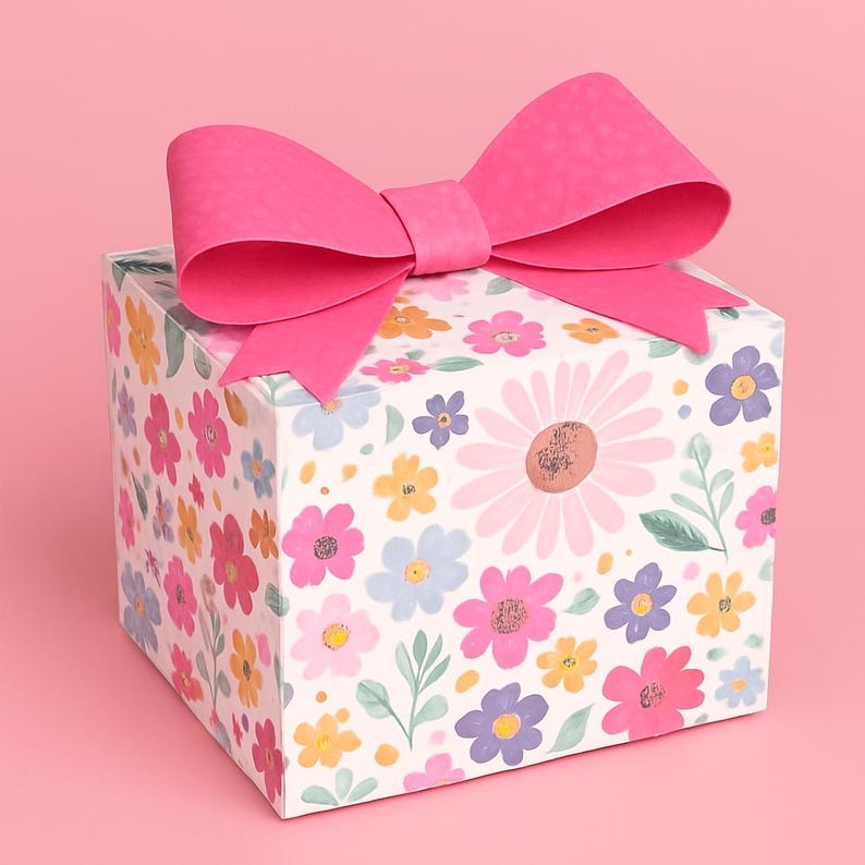 May include: A square gift box with a floral pattern and a large pink bow on top. The box is covered in a white background with colorful flowers in pink, yellow, blue, and purple. The bow is a vibrant pink.