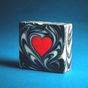 Jabón artesanal en frío con corazón rojo y espirales blancos y negros, regalo romántico para el cuidado personal.