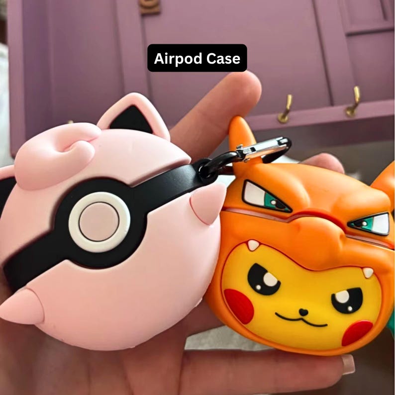 May include: Two colorful Airpod cases. One is pink with black accents and a white circle, resembling a character. The other is orange and yellow, also resembling a character. The text "Airpod Case" is in a black rectangle.