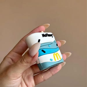 May include: A white, blue, and yellow novelty item with the text "McFlurry" in black. The item has a cartoon design and the McDonald's golden arches logo. The item is held in a hand.