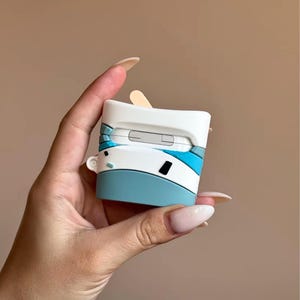 May include: A white, blue, and black AirPod case with a unique design. The case has a light blue base, white top, and blue accents. The case is held in a hand against a neutral background.