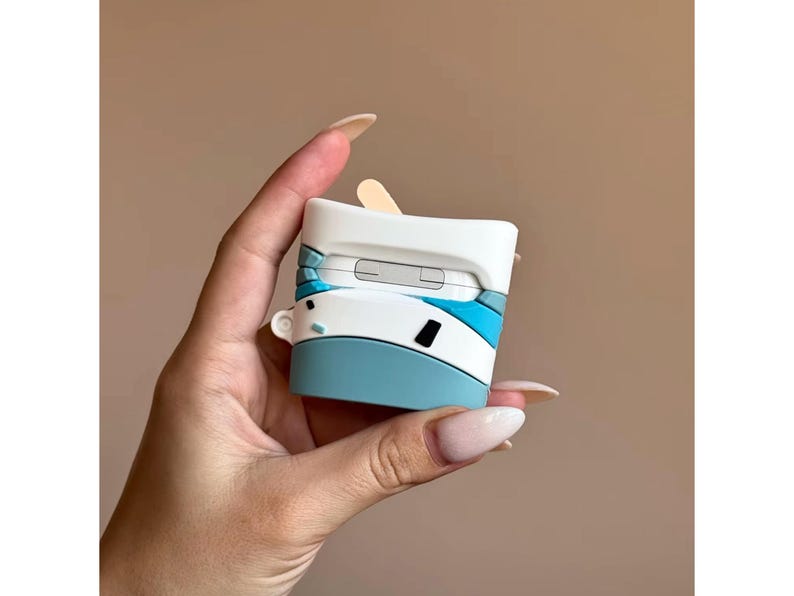 May include: A white, blue, and black AirPod case with a unique design. The case has a light blue base, white top, and blue accents. The case is held in a hand against a neutral background.