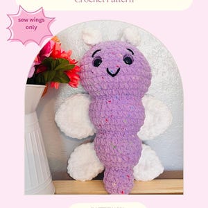 May include: A crocheted dragonfly toy in shades of purple and white. The dragonfly has a textured body with colorful flecks, white wings, and small white antennae. The text "TWINKLEWING THE DRAGONFLY Crochet Pattern" is displayed at the top.