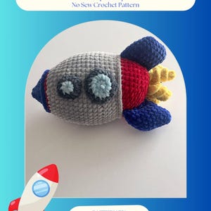May include: A handmade crochet spaceship toy in gray, red, blue, and yellow. The toy has large, round eyes and a detailed design. Text on the image reads "Benny Blastoff the Spaceship No Sew Crochet Pattern" and "Pattern by Yarnimalsbytoni".