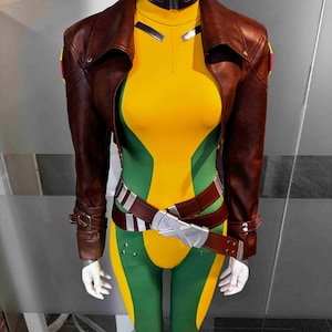 May include: A costume on a mannequin featuring a brown leather jacket, a yellow and green bodysuit, and a brown belt with a silver buckle. The jacket has a collar and the bodysuit has a high neck.