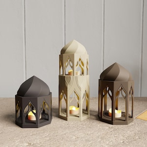 May include: Three decorative candle lanterns in varying shades of brown and beige. Each lantern has a domed top and intricate cut-out designs. Lit candles inside cast a warm glow, creating a cozy ambiance. The lanterns are arranged on a neutral surface.