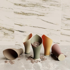 May include: A collection of colorful, cone-shaped containers with textured exteriors. The containers are in shades of beige, green, orange, and pink, some filled with brown material. The cones are arranged on a marble surface.