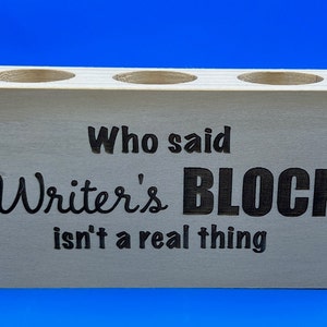 May include: Wooden pencil holder with three holes and the text "Who said Writer's BLOCK isn't a real thing"