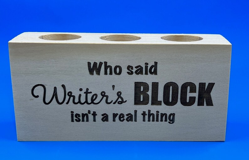 May include: Wooden pencil holder with three holes and the text "Who said Writer's BLOCK isn't a real thing"
