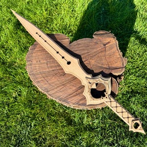 May include: A light brown wooden sword with detailed cut-out patterns on the hilt and blade. The sword rests on a wooden tree stump, set against a background of green grass.