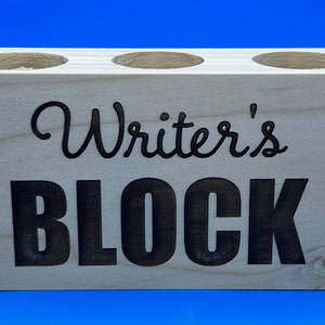 May include: Wooden pencil holder with three slots and the text "Writer's Block" in black lettering.