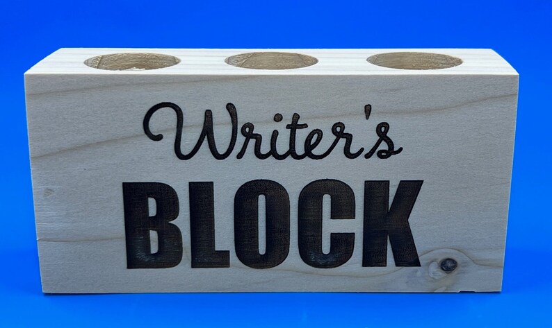 May include: Wooden pencil holder with three slots and the text "Writer's Block" in black lettering.