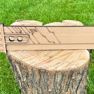 May include: A wooden Buster Sword replica, featuring a detailed design with a rectangular blade and a handle with a series of circular accents. The sword is displayed on a tree stump against a backdrop of green grass.