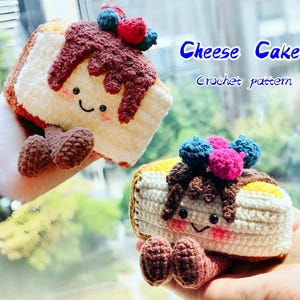 Puede incluir: Dos porciones de tarta de queso de ganchillo con caras sonrientes, glaseado de chocolate y cobertura de bayas. El texto "Cheese Cake Crochet pattern" es visible. Los postres hechos a mano tienen bases color crema y costras marrones.