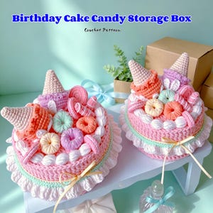 May include: Two handmade crochet birthday cake candy storage boxes. The cakes are pink with white frosting, adorned with colorful crochet candies, and topped with ice cream cone shapes. The text "Birthday Cake Candy Storage Box" and "Crochet Pattern" are visible.